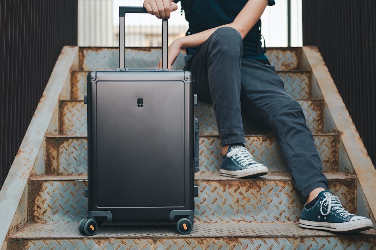 A cropped photo of a man sitting on rusty stairs while holding black luggage. 