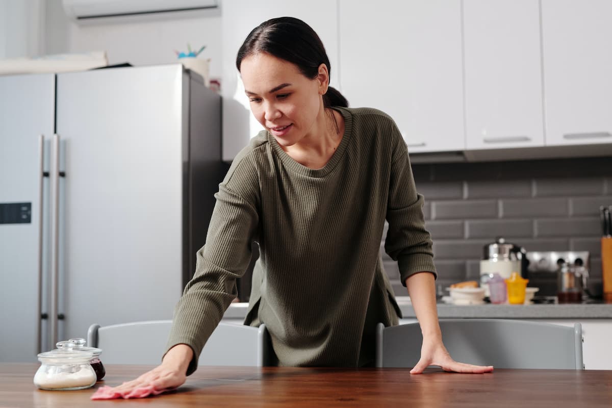 A woman is wiping the table in the kitchen. 