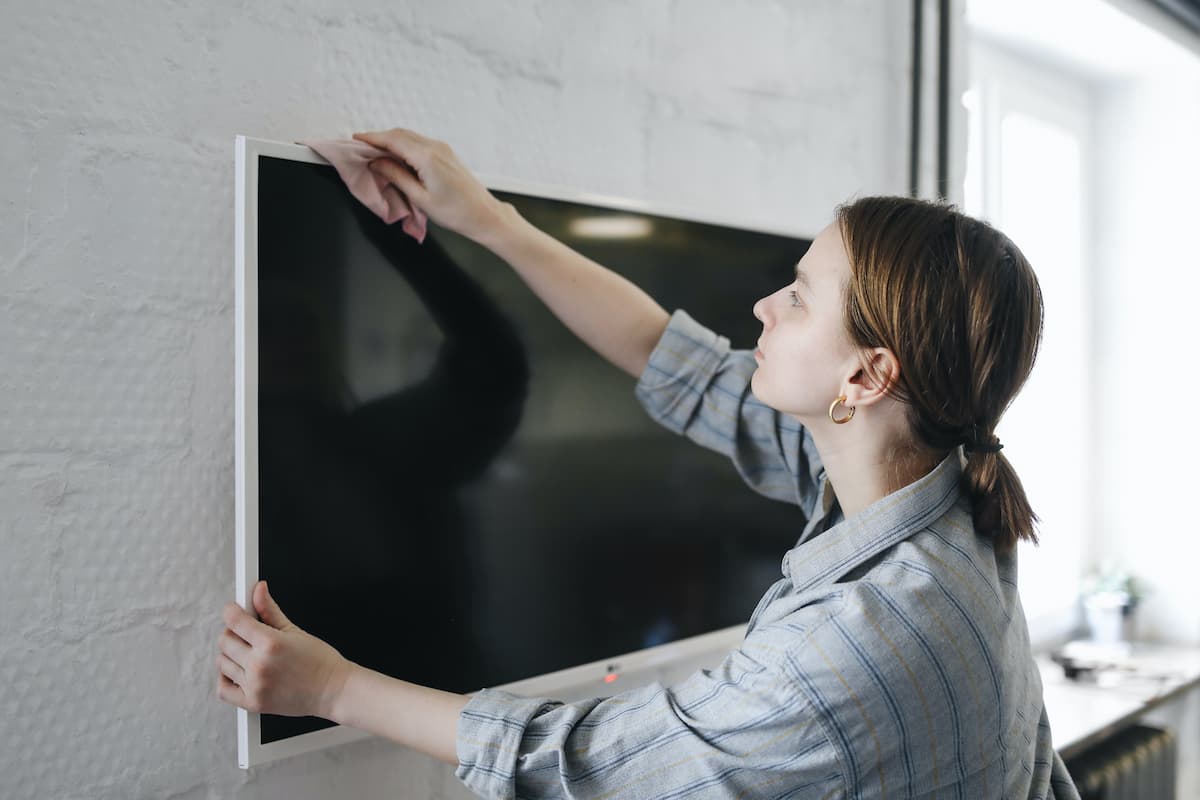 A woman wearing a folded long sleeve is wiping the television with a cloth. 