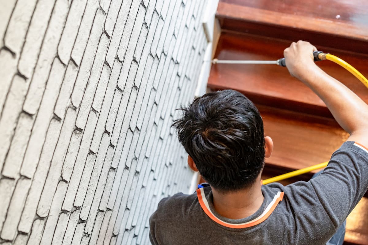 An exterminator spraying insecticide between the stairs and wall. 