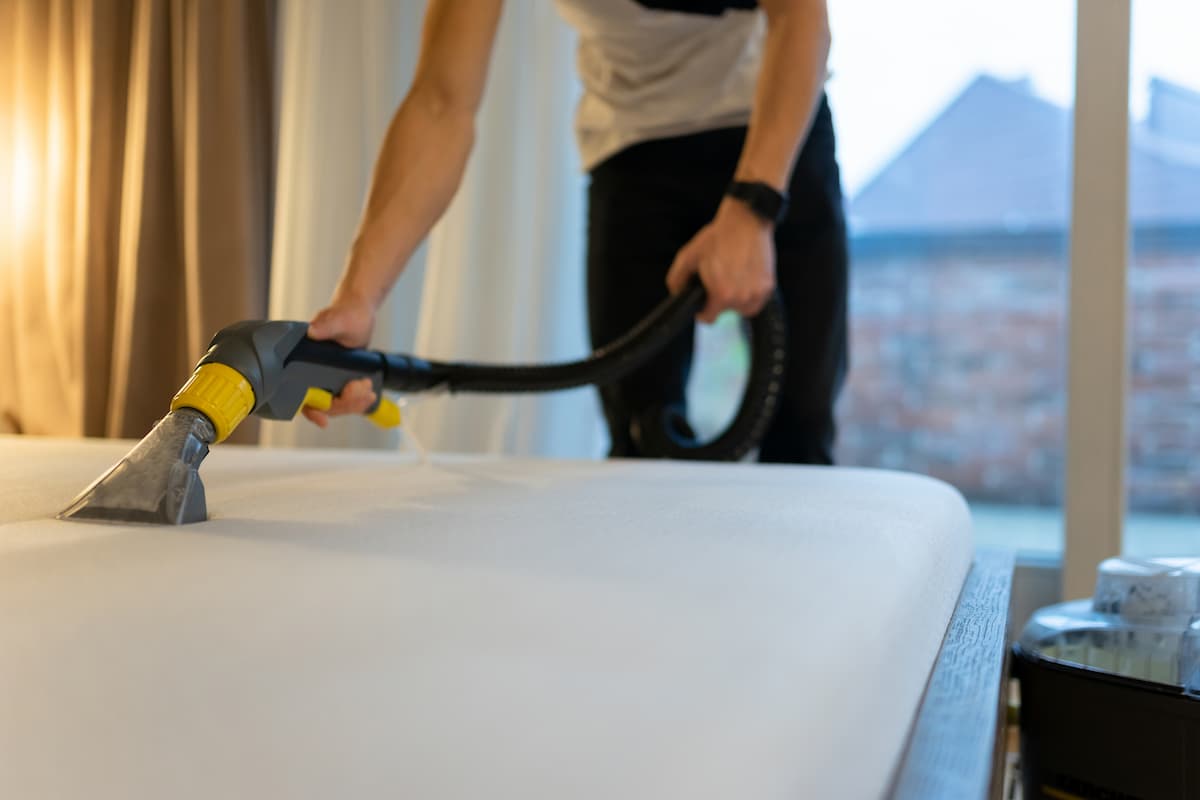 A man cleaning the bed with a vacuum. 