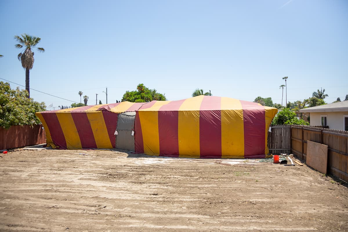 A real estate property covered by a yellow and red striped fumigation tent.