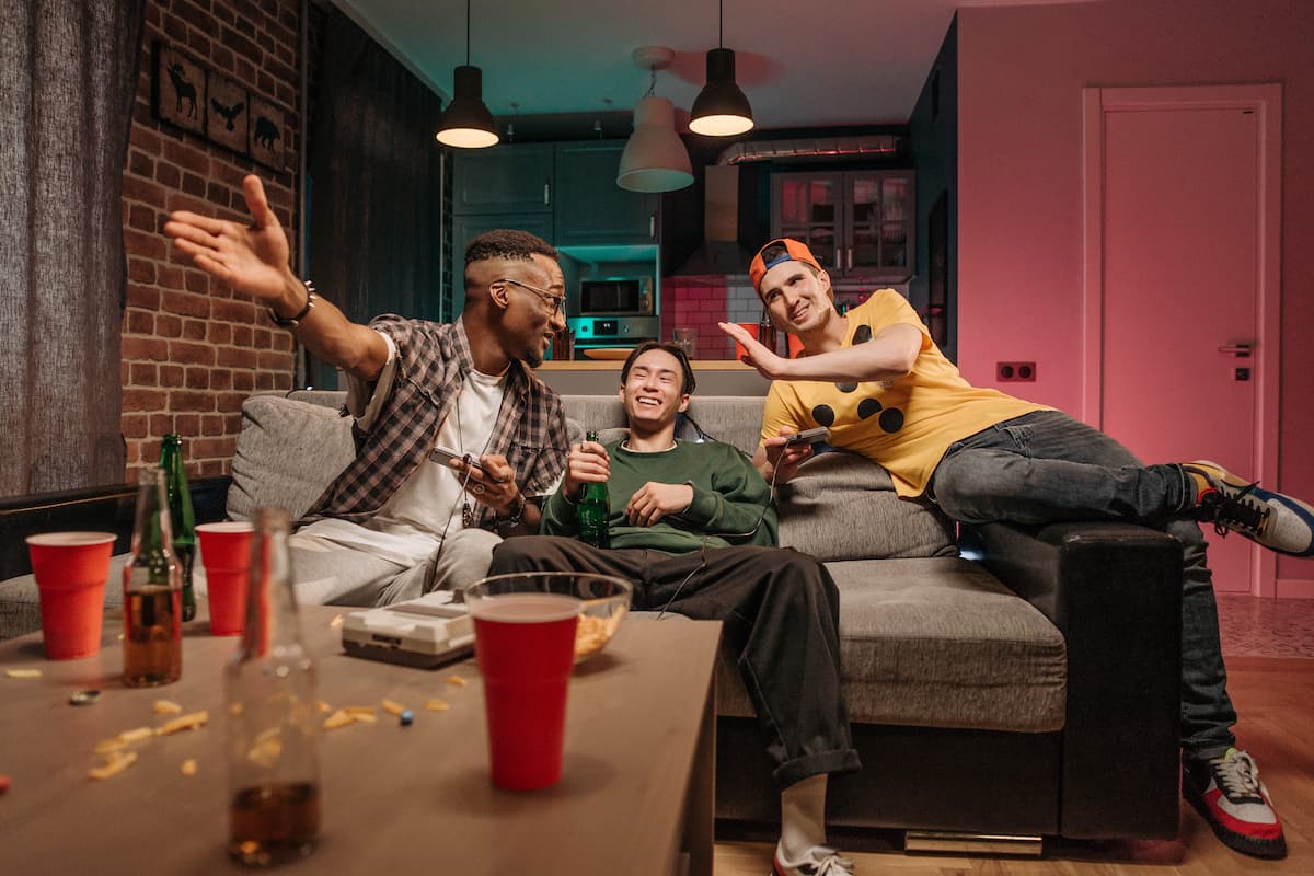 Three men hanging out in the living room while playing video games and drinking beer. 