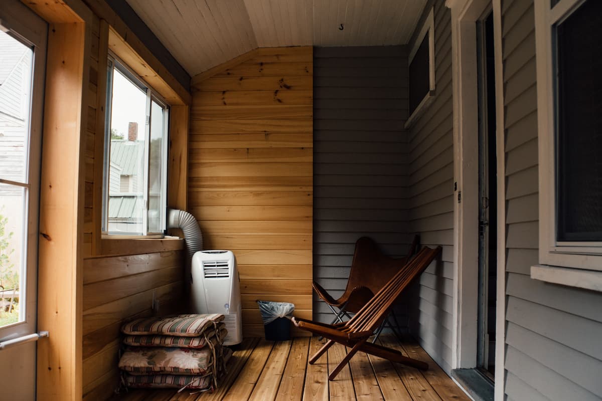 The interior of a wooden house with wooden chairs, heater. and a folding mattress.