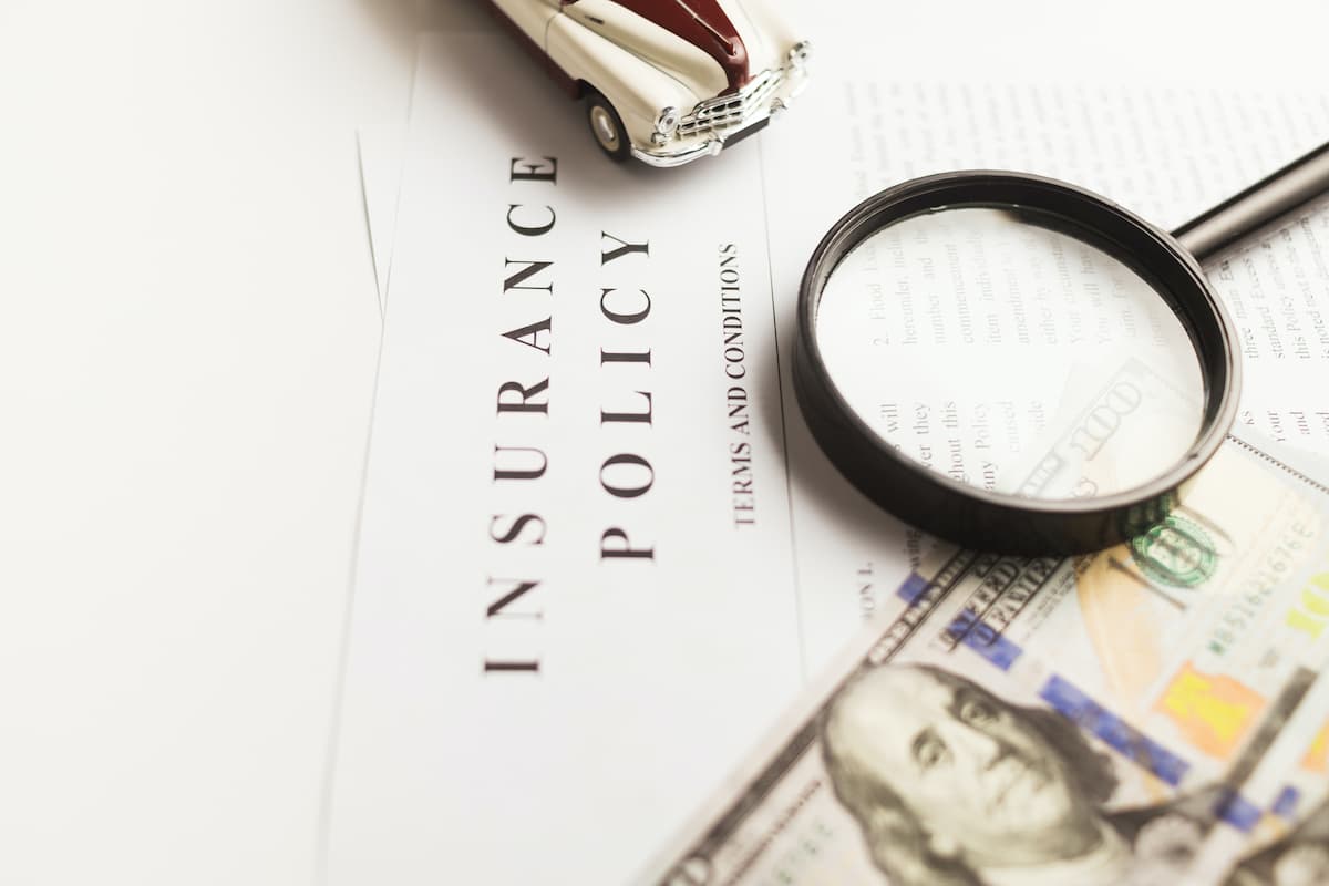 On the Insurance Policy document, there is a magnifying glass, a toy car, and a $100 US bill.