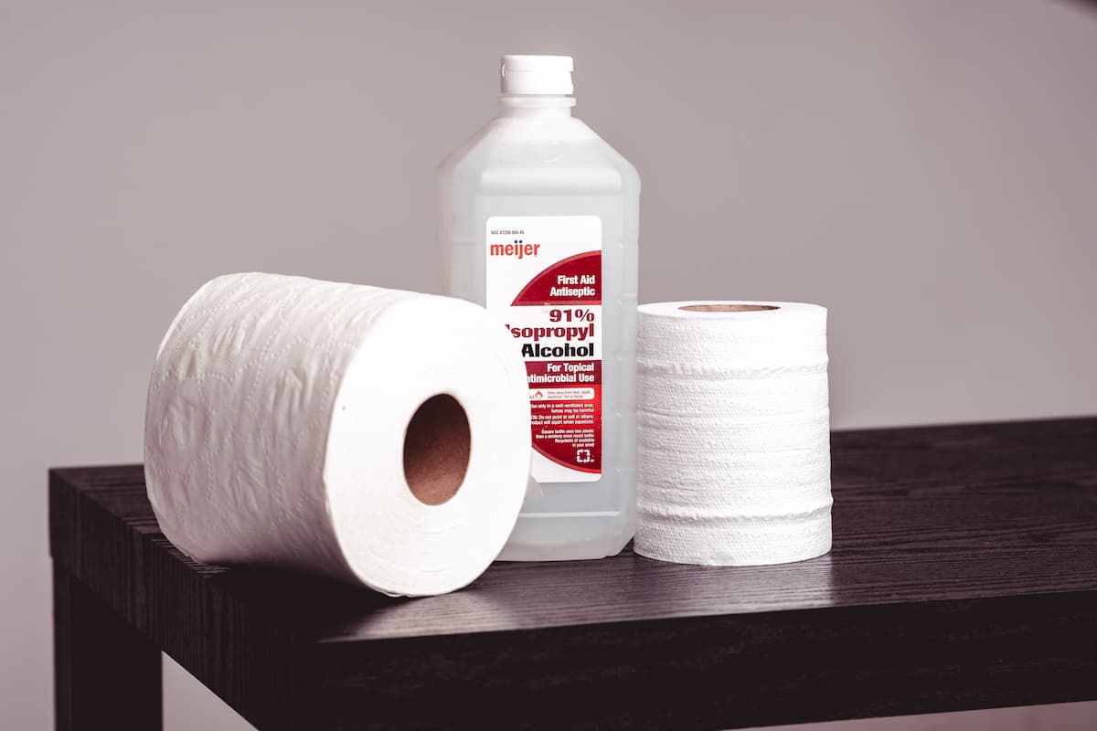 A bottle of isopropyl alcohol between two tissue rolls on a brown wooden table.