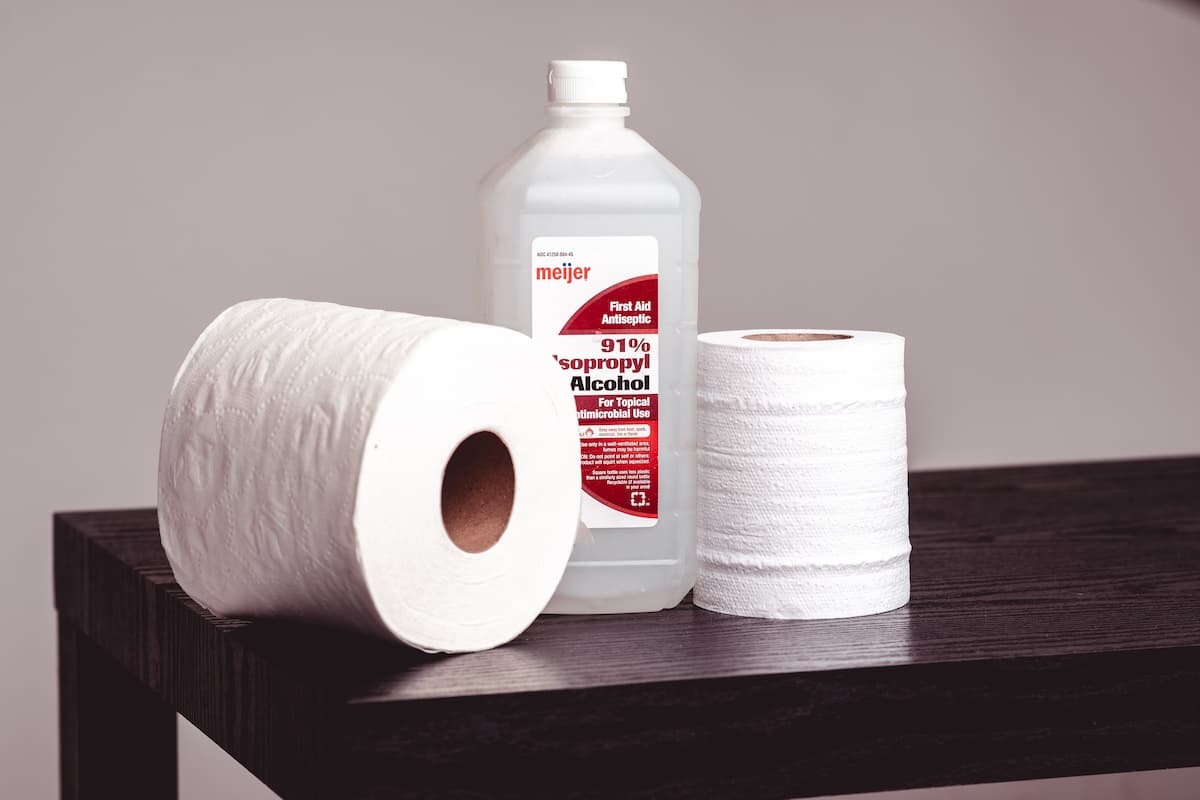 A bottle of isopropyl alcohol between two tissue rolls on a brown wooden table. 