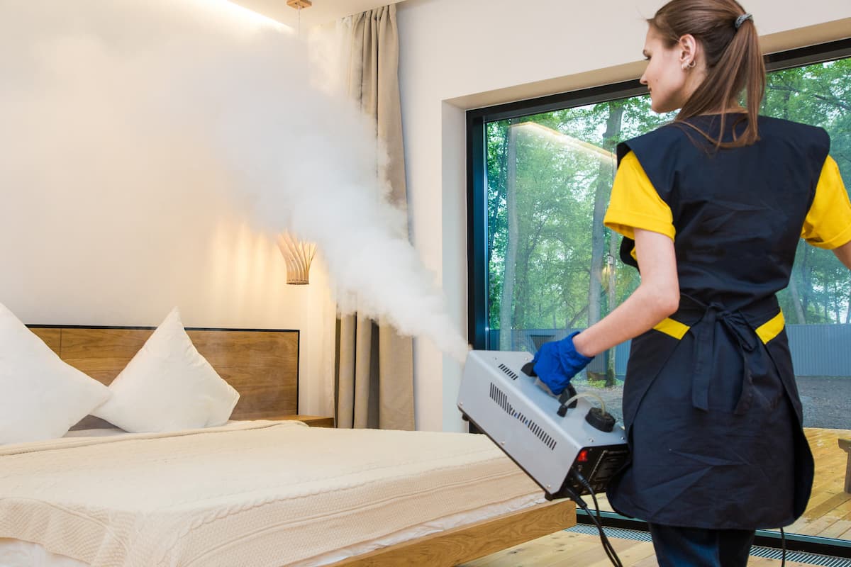 A woman exterminator is using steam and a heater in the bedroom.