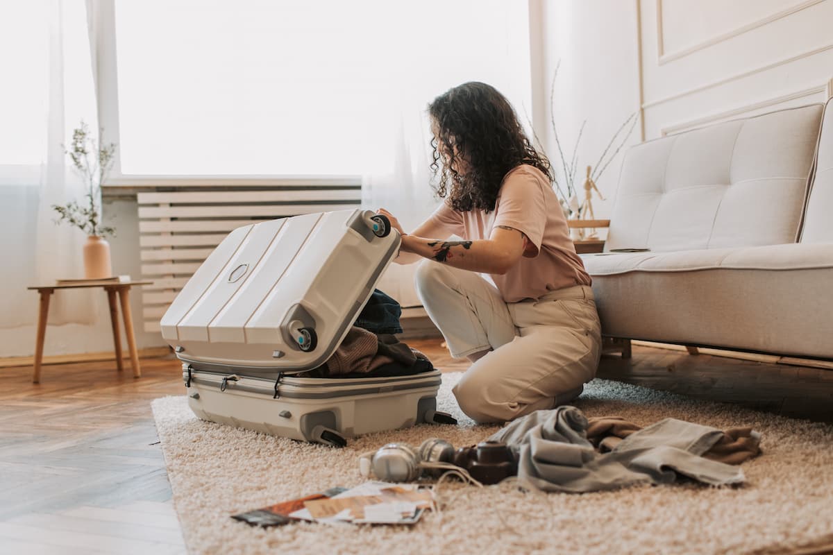 A woman is packing her luggage on the carpeted floor.