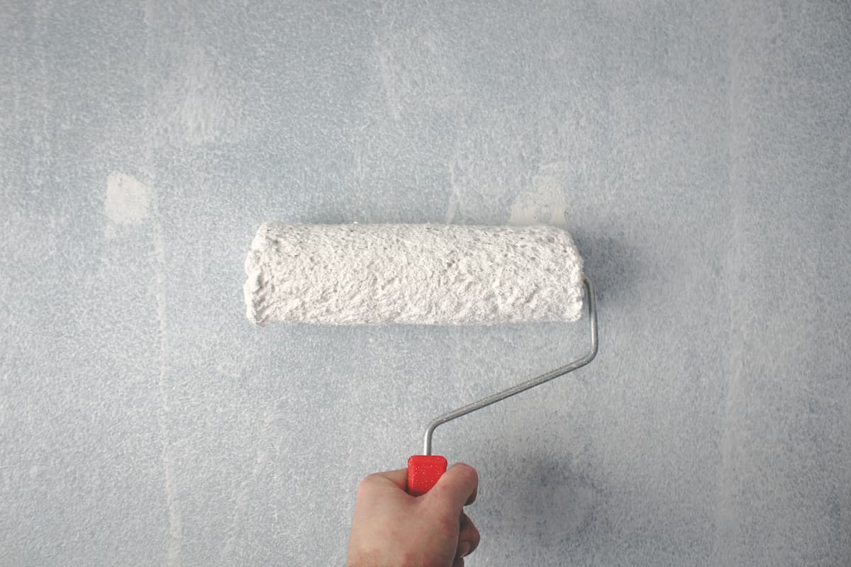 A person using a paint roller to apply white paint to a wall. 