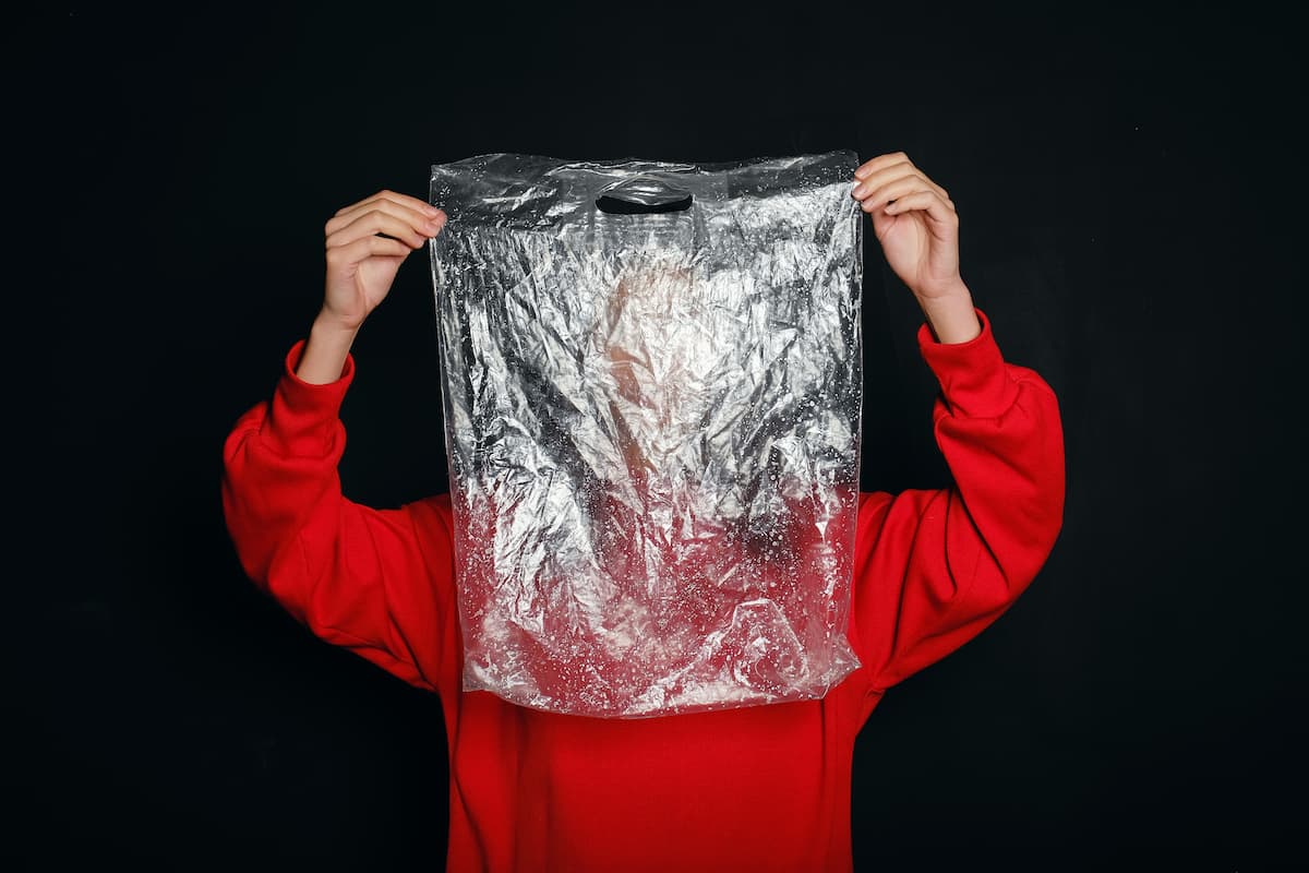 A woman in a red sweater is holding a plastic bag with a black background. 