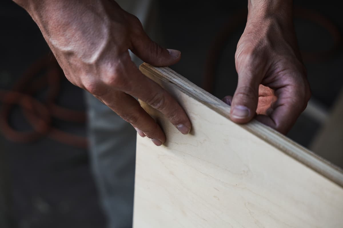 A man's hands are holding a piece of plywood.