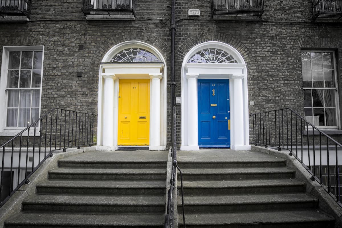 Two apartments with yellow and blue doors are depicted in a photo of an apartment complex.