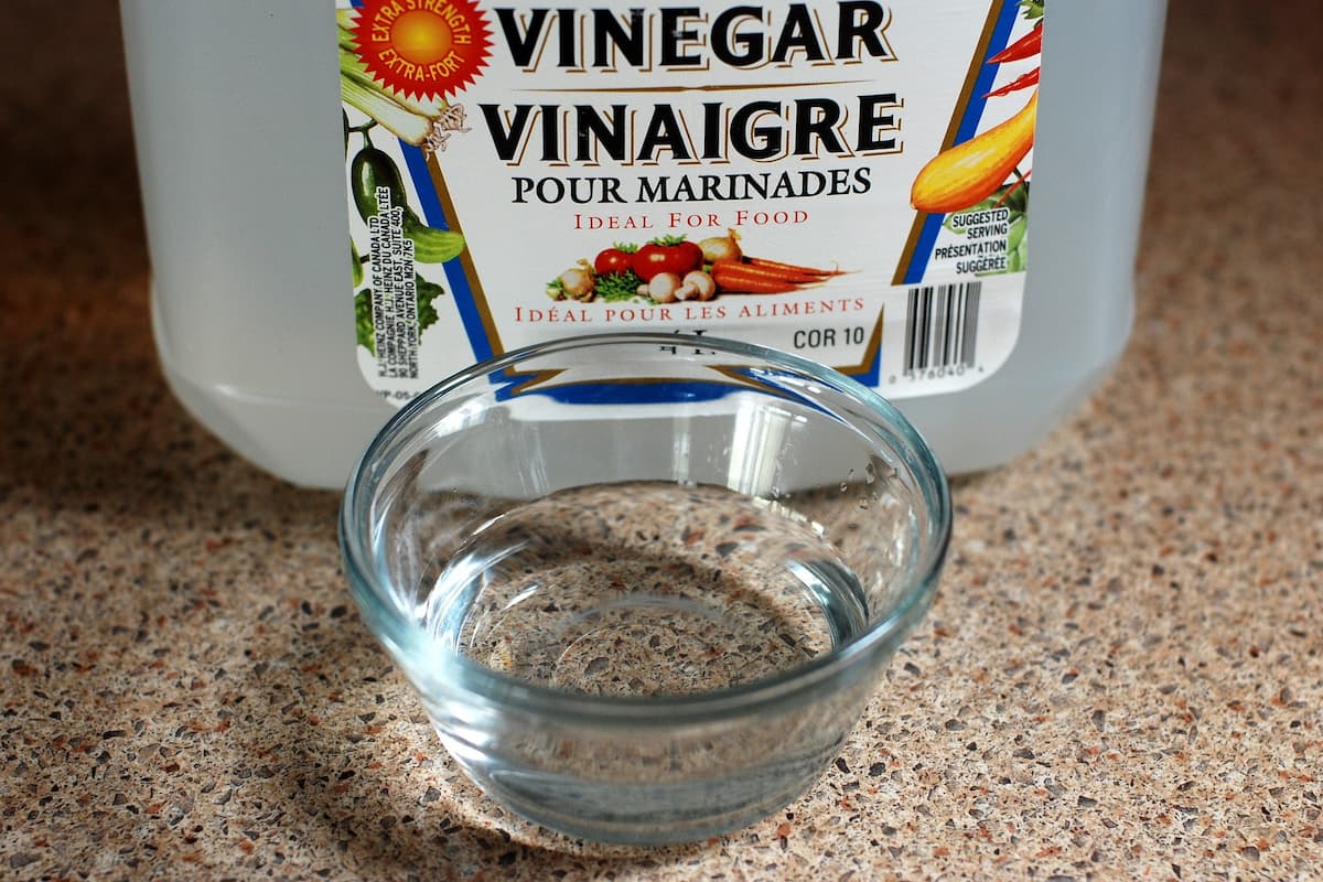 A close-up of a saucer with vinegar and a bottle of vinegar in the back.