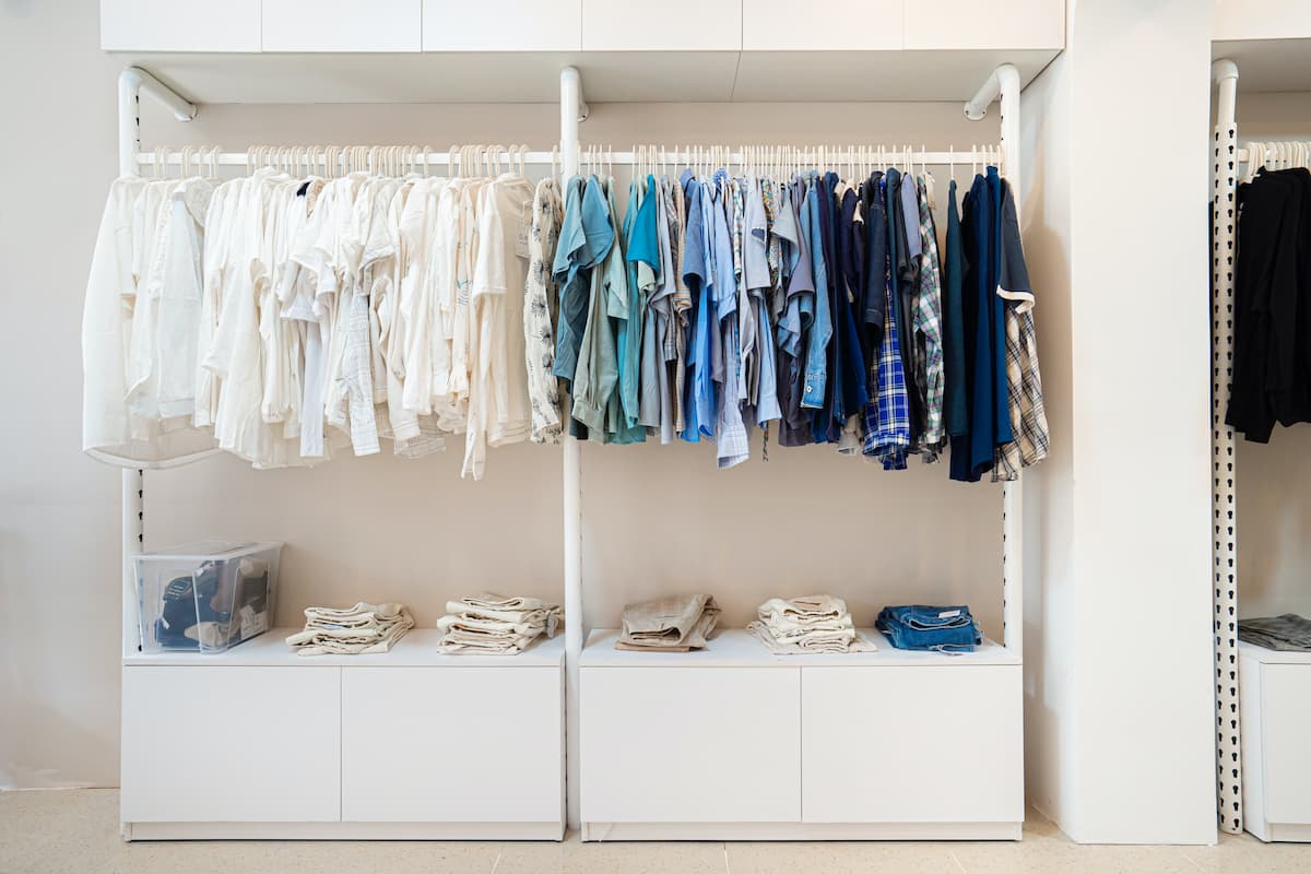 A white cabinet holds a wardrobe with white and blue garments hanging on it.