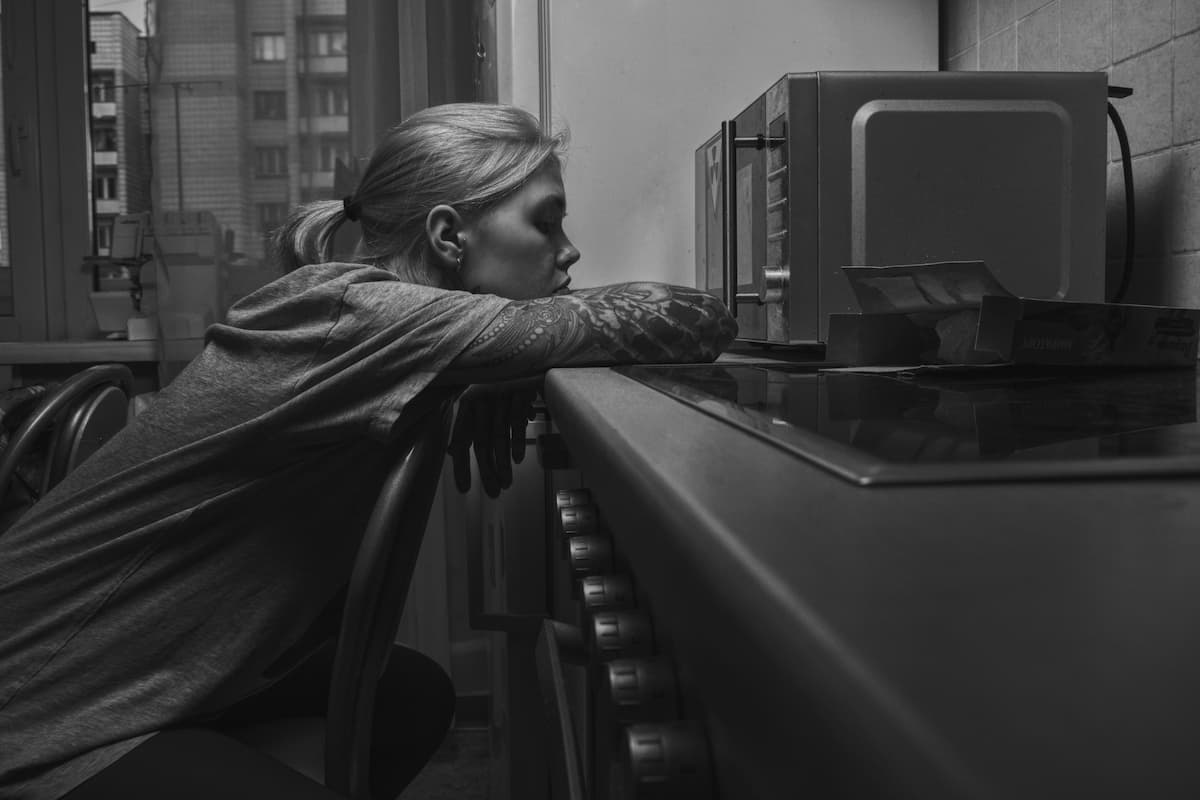 A black and white photo of a woman sitting in front of the microwave. 